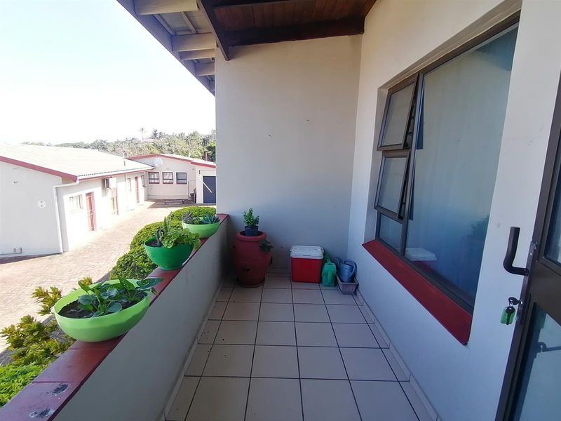 A covered balcony featuring tiled flooring, a timber ceiling, and a top-hung window, offering an outdoor space overlooking the complex grounds.