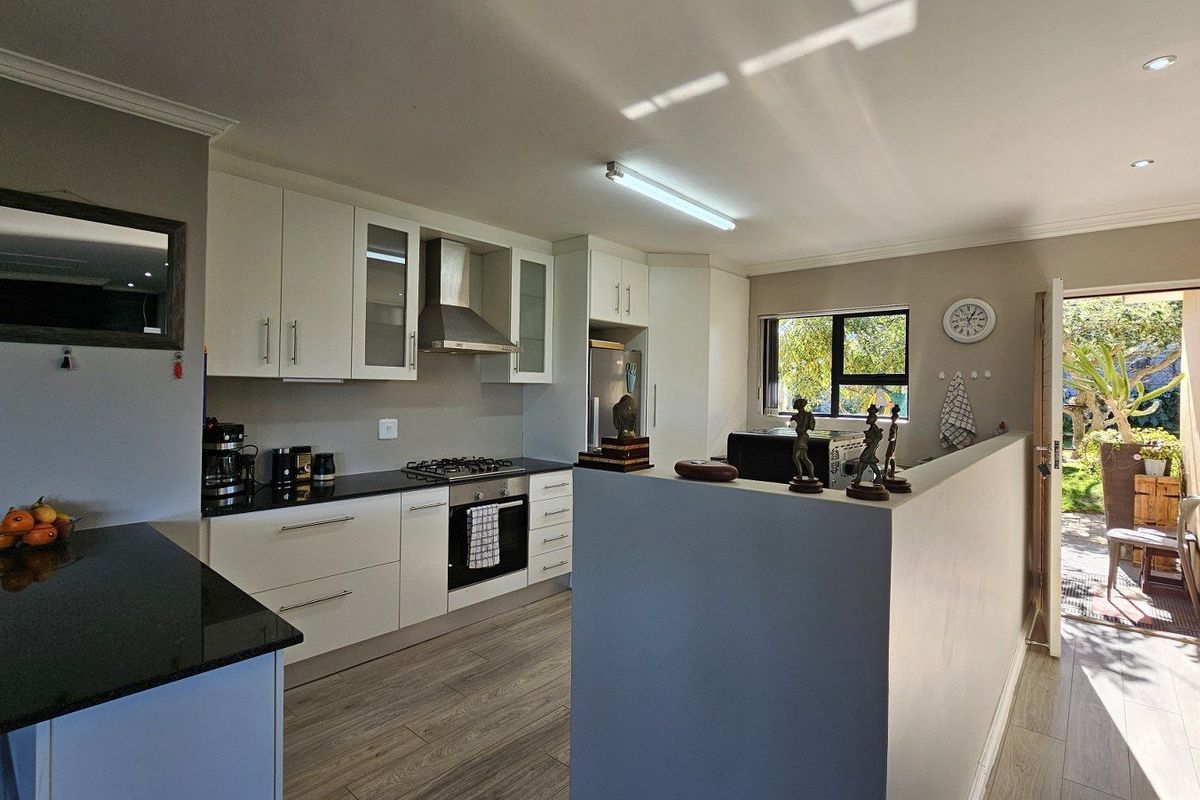 Modern kitchen featuring white cabinetry, black granite countertops, built-in gas hob, stainless steel extractor fan, and direct access to the outdoor patio area.