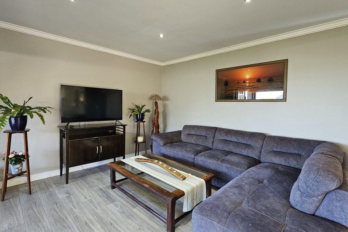 A comfortable living room featuring neutral wall tones, crown molding, and modern wood-look flooring.