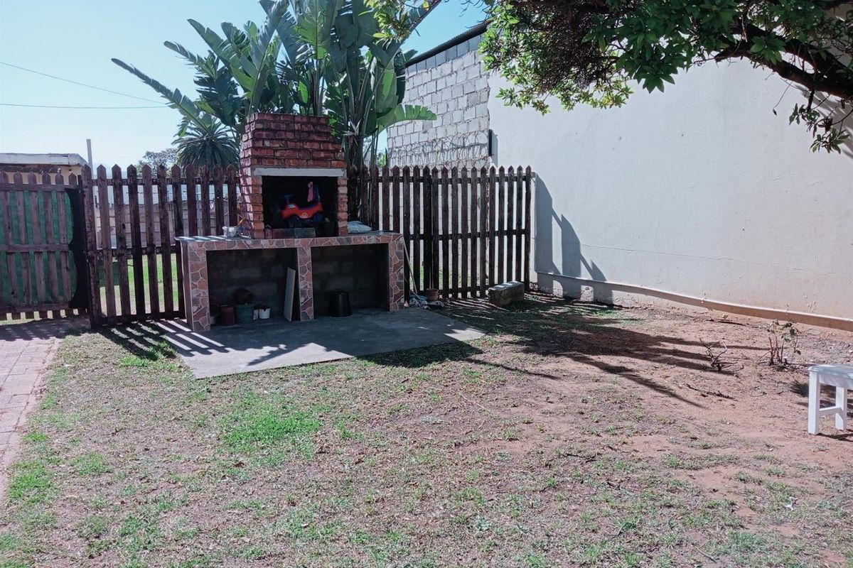 A rear garden area featuring a built-in brick braai or barbecue station, enclosed by timber fencing and adjacent to a boundary wall.