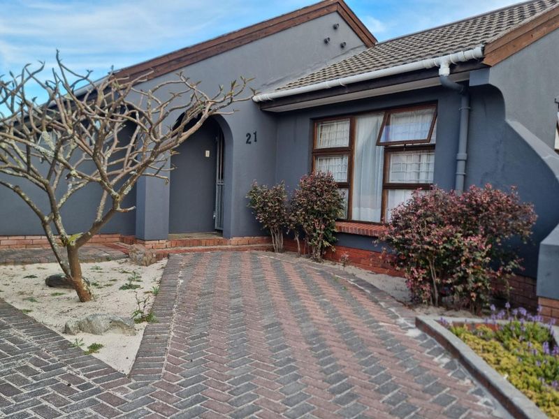 Front elevation of a single-story house featuring a paved driveway, brick foundation, and dark grey exterior walls with aluminium window frames.