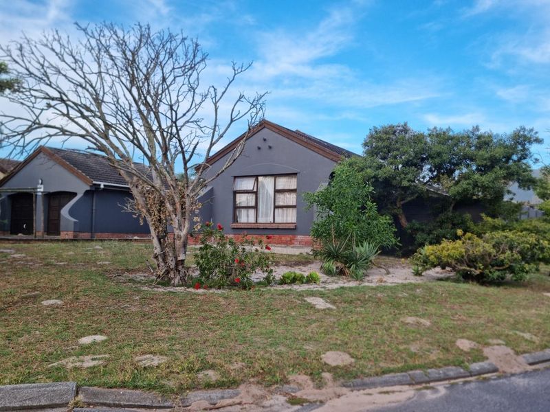 Front view of a single-story residential house featuring a dark grey exterior finish, tiled roof, and established garden area.