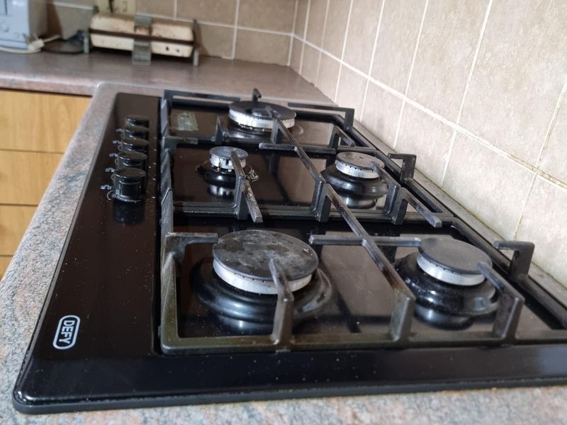 Close-up view of a built-in black gas hob set into a laminate countertop with a tiled backsplash in a kitchen.