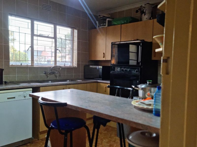 A functional kitchen featuring built-in cabinetry, laminate countertops, a stainless steel sink, and a built-in oven, with tiled walls and a window with security bars.