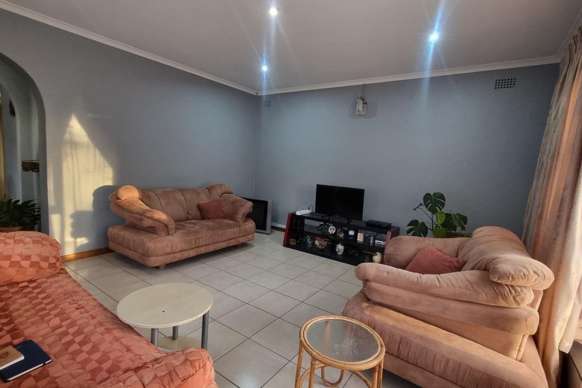 A spacious living room featuring neutral tiled flooring, recessed downlighting, and a classic archway leading to the hallway.