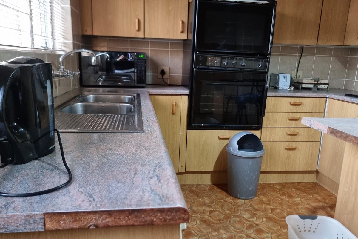 A functional kitchen featuring laminate cabinetry, a double bowl stainless steel sink, and a built-in double oven with tiled splashbacks.