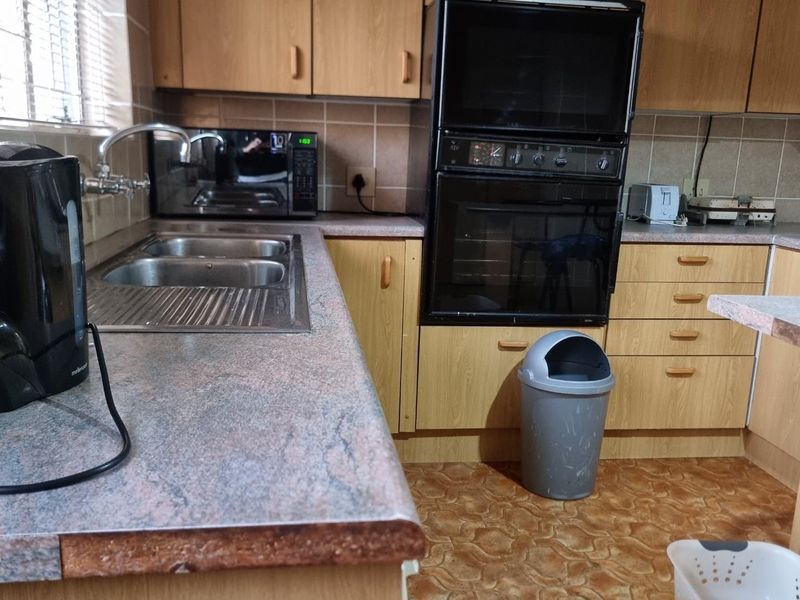 A functional kitchen featuring laminate cabinetry, a double bowl stainless steel sink, and a built-in double oven with tiled splashbacks.