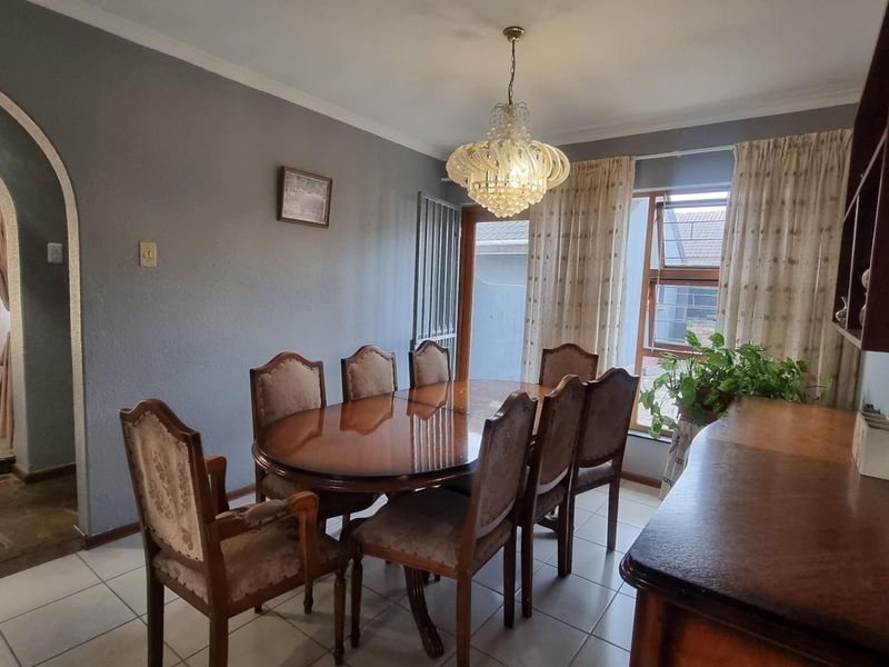 A dining room featuring tiled flooring, a decorative crystal chandelier, and an arched entryway leading to an adjacent living space.