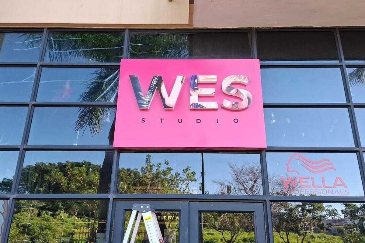 Exterior view of a commercial studio storefront featuring large glass panel windows, a prominent pink signage board, and a central glass entrance door.
