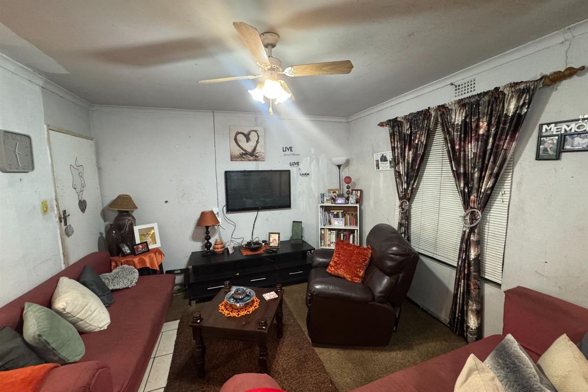 A living room featuring a ceiling fan and tiled flooring, requiring cosmetic updates to the wall finishes.