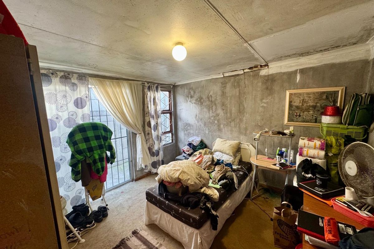 A bedroom featuring a sliding glass door with security gate, concrete-finish walls, and ceiling panels requiring maintenance and cosmetic repair.