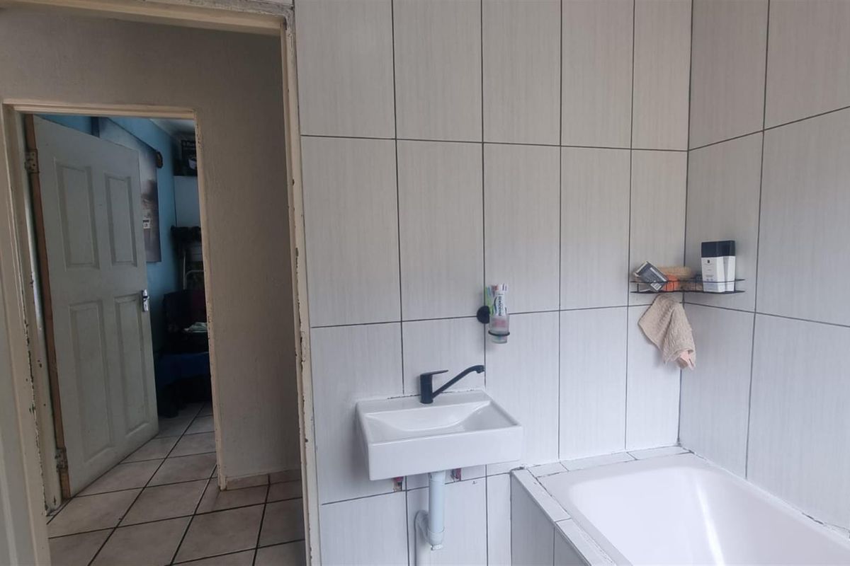 A functional bathroom featuring white wall tiles, a built-in bathtub, and a wall-mounted basin with modern black tapware.