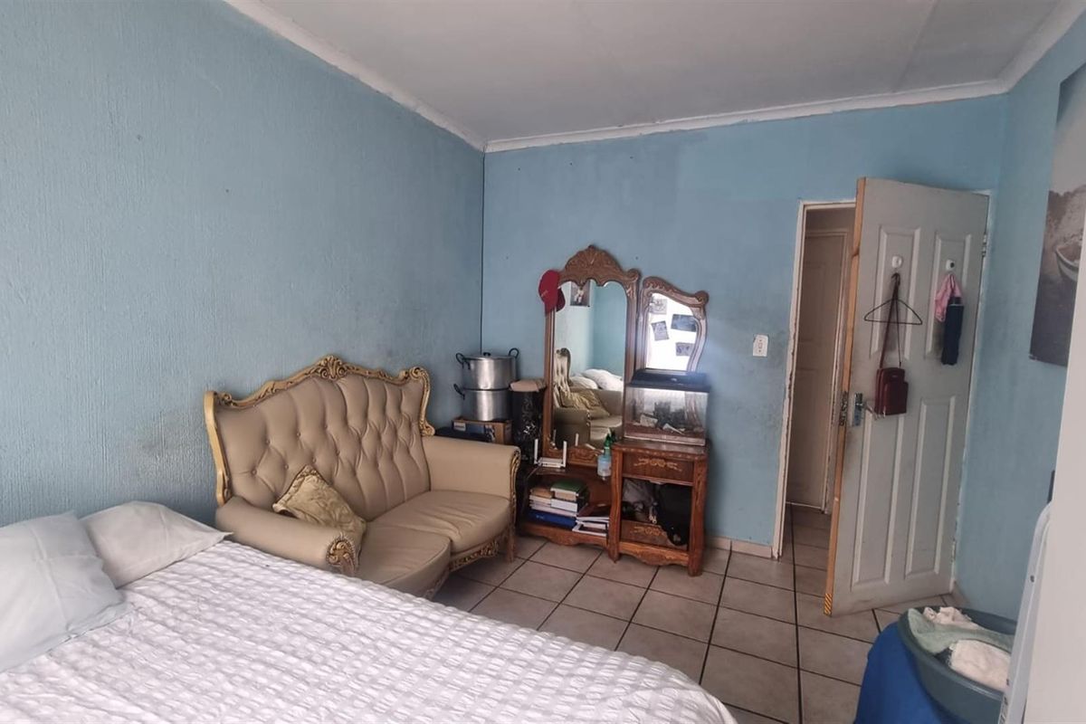 A bedroom featuring tiled flooring and blue painted walls, providing a functional space with direct access to an adjacent room.