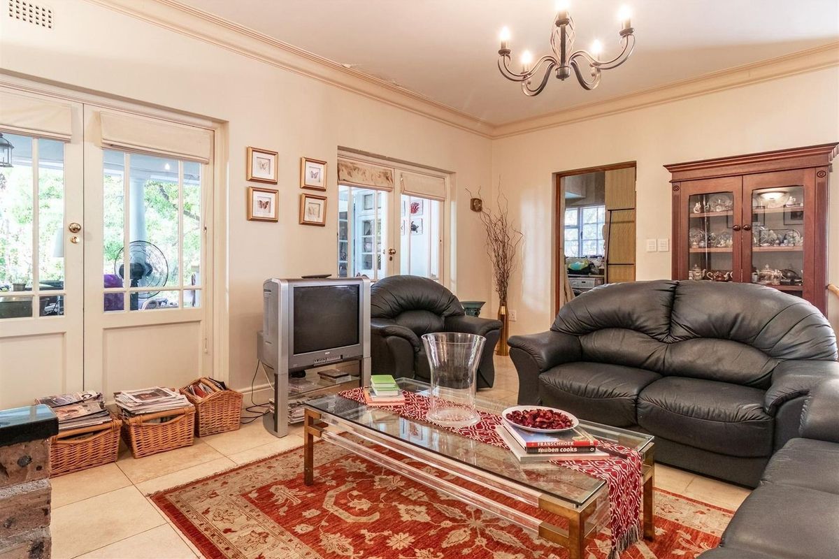A spacious living room featuring tiled flooring, crown molding, a classic chandelier, and double glass doors providing access to the patio.
