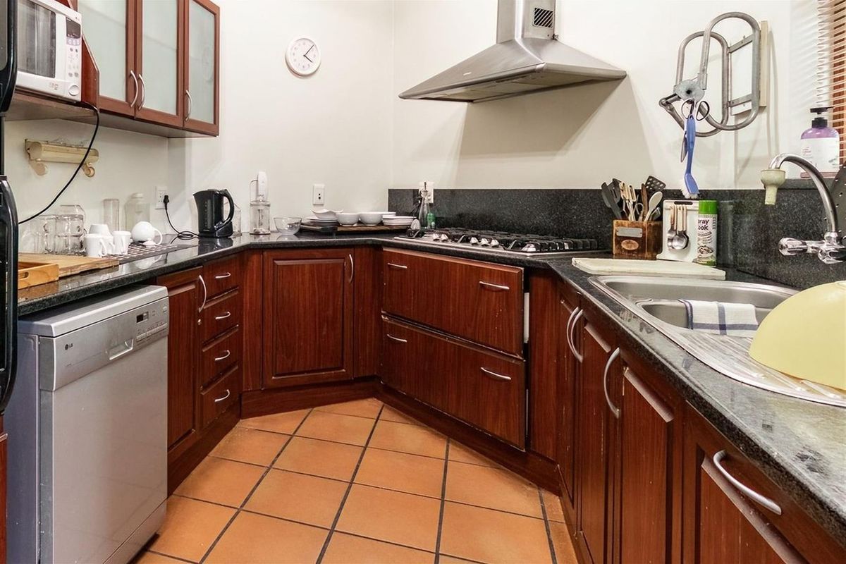 A functional kitchen featuring dark wood cabinetry, granite countertops, a gas hob, stainless steel extractor fan, and tiled flooring.