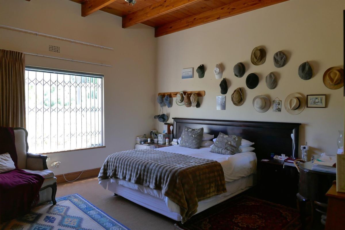 A spacious bedroom featuring exposed timber ceiling beams, a large window with security bars, and neutral wall finishes.
