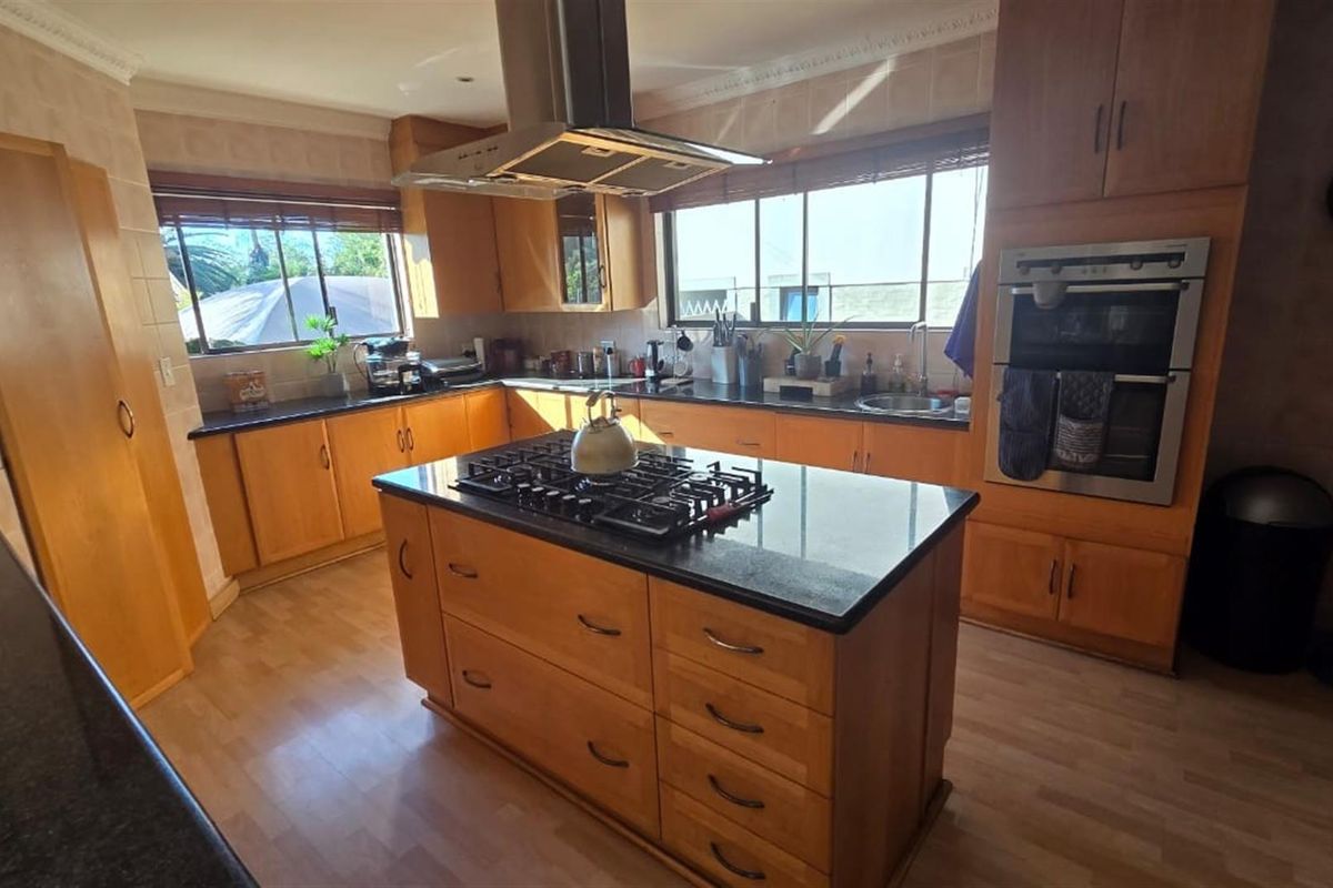 A functional kitchen featuring wooden cabinetry, granite countertops, a central island with a gas hob, and built-in double oven appliances.