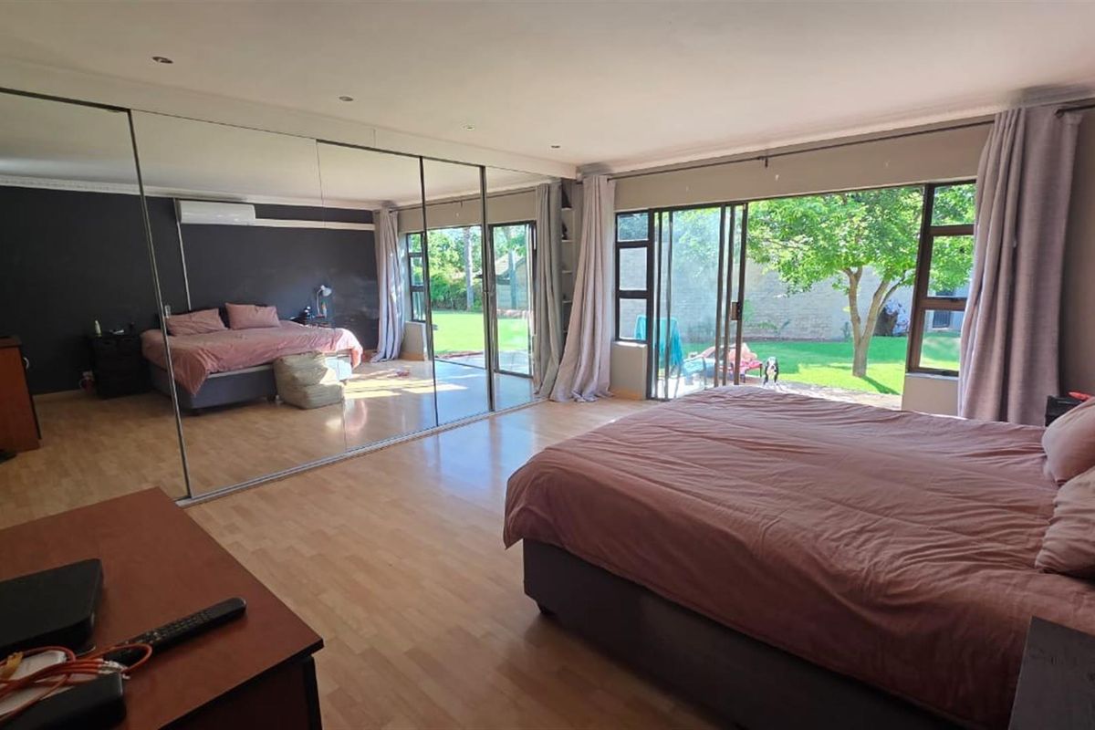 Spacious bedroom featuring large mirrored sliding wardrobes, laminate flooring, and sliding glass doors providing direct access to the garden.