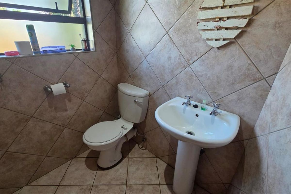 A functional bathroom featuring a pedestal basin, toilet, and full-height ceramic wall tiling.