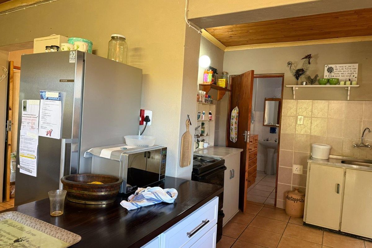 A functional kitchen area featuring tiled flooring, timber ceiling accents, and built-in cabinetry, with an adjacent doorway leading to a bathroom.
