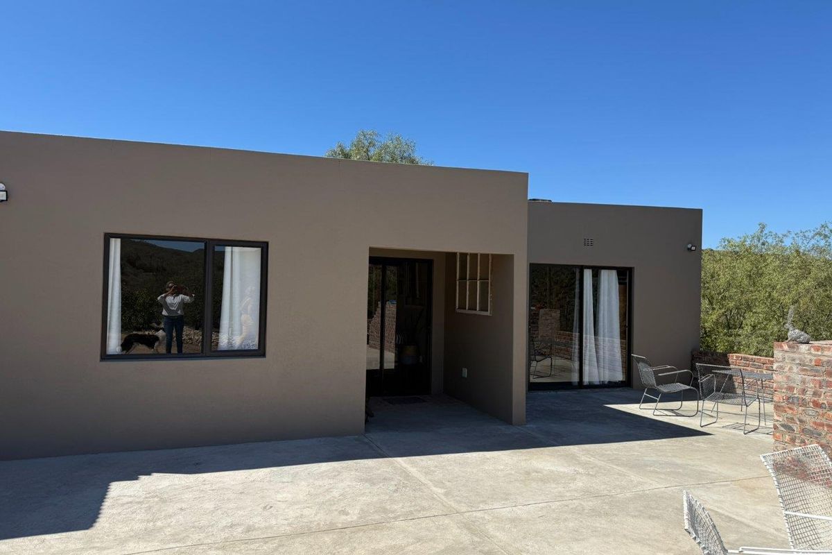 Rear exterior view of the property featuring a spacious concrete patio, modern sliding glass doors, and a brick retaining wall set against a landscape.