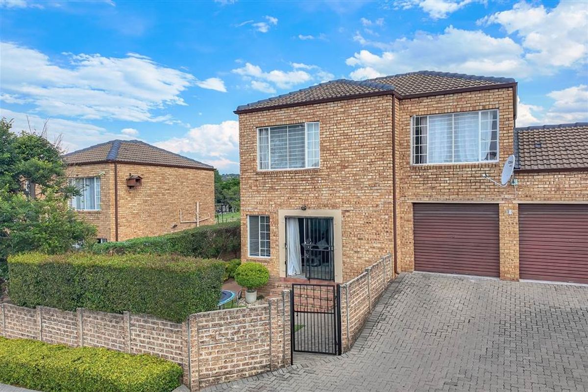 A well-maintained double-story townhouse featuring a face brick exterior, paved driveway, and double garage with secure gated access.