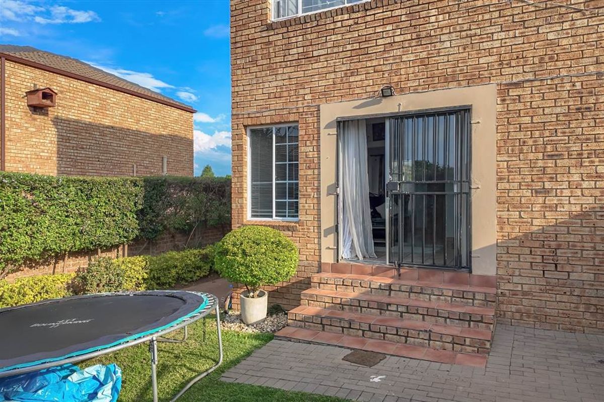 Rear exterior view of the townhouse featuring a brick facade, paved patio area, and direct access to the living space via a sliding door.