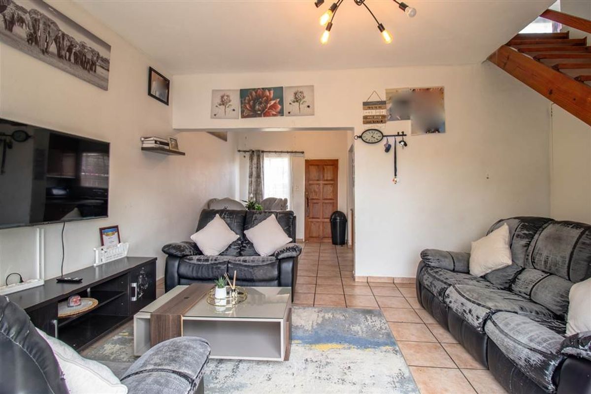 Open-plan living area featuring tiled flooring, a wooden staircase, and direct access to the front entrance.