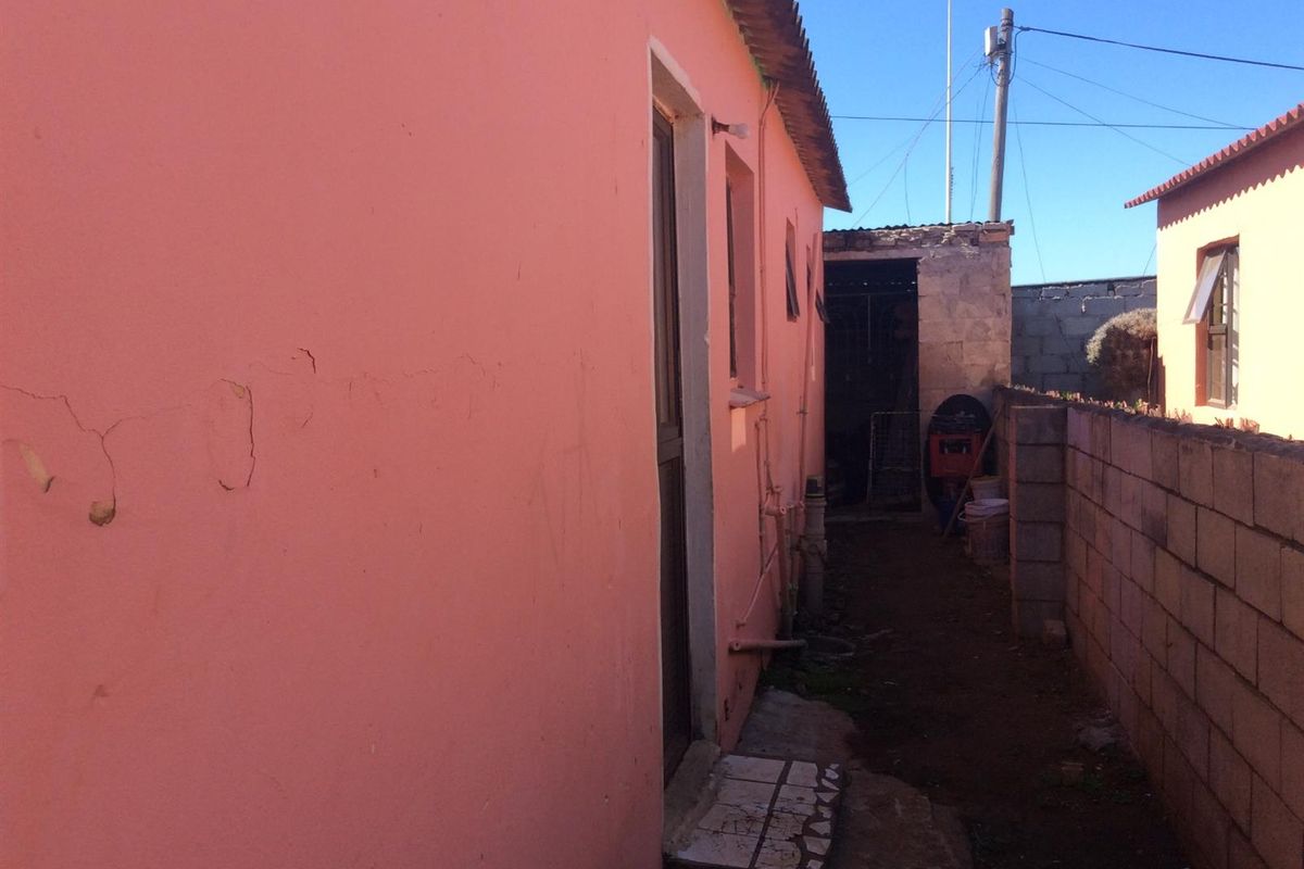 Side passage of the property featuring a concrete block boundary wall and exterior wall with visible plaster cracking and paint deterioration.