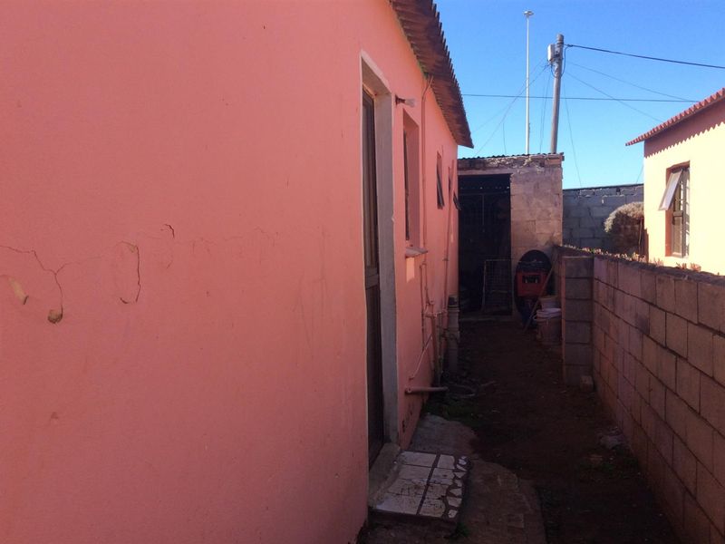 Side passage of the property featuring a concrete block boundary wall and exterior wall with visible plaster cracking and paint deterioration.