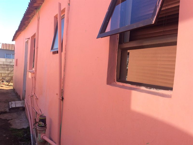 Side view of the property exterior showing painted masonry walls, top-hung windows, and exposed external plumbing infrastructure.