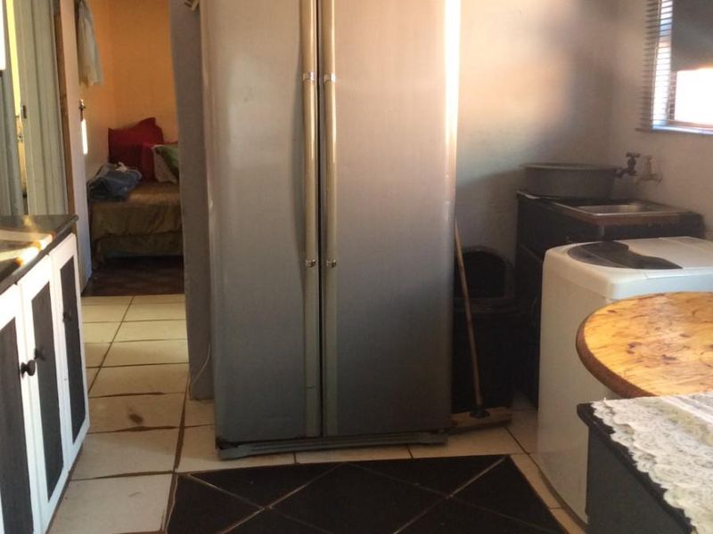 A functional kitchen area featuring tiled flooring, built-in cabinetry, and a window with blinds, showing signs of wear and requiring cosmetic updates.
