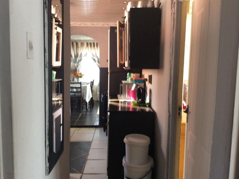 A narrow kitchen area featuring built-in cabinetry and tiled flooring, leading through an archway into an adjacent dining space.