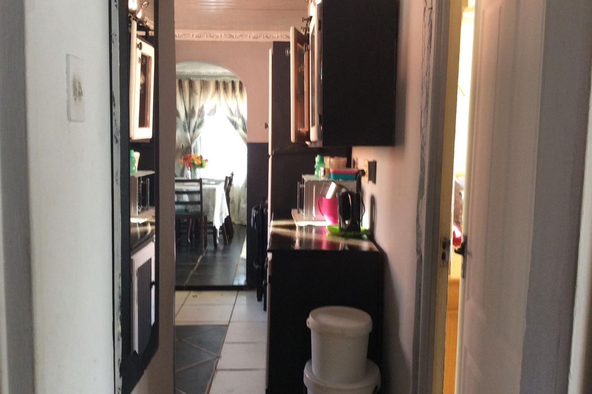 A narrow kitchen area featuring built-in cabinetry and tiled flooring, leading through an archway into an adjacent dining space.