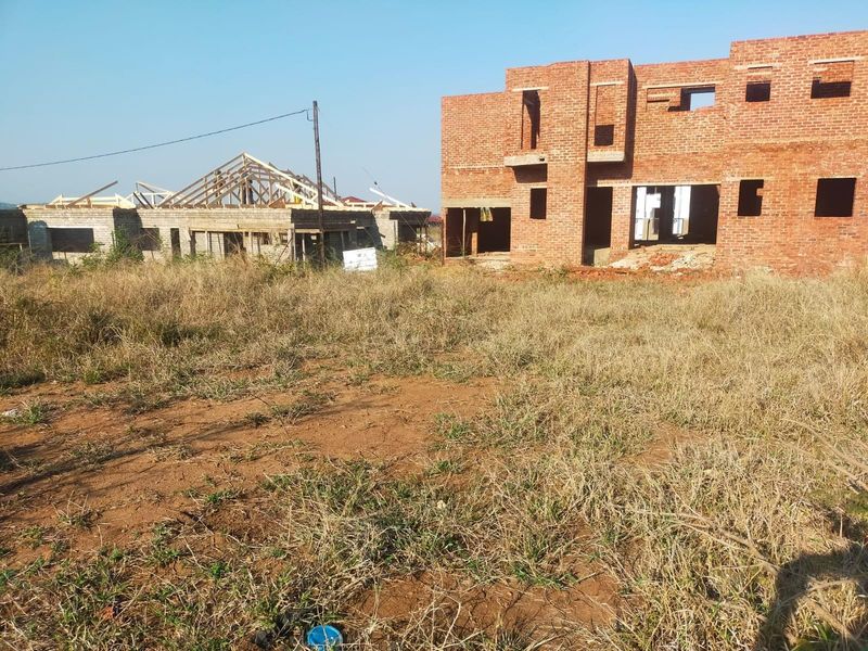 A vacant residential plot featuring an ongoing construction project with exposed brickwork and timber roof framing.