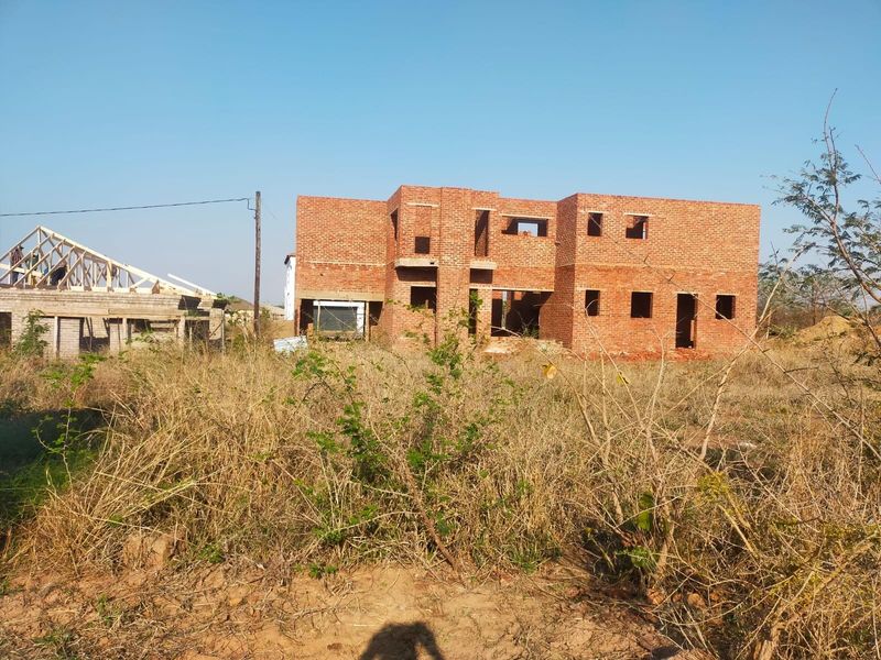 A residential property under construction featuring an exposed brick structure and timber roof trusses on a vacant plot.