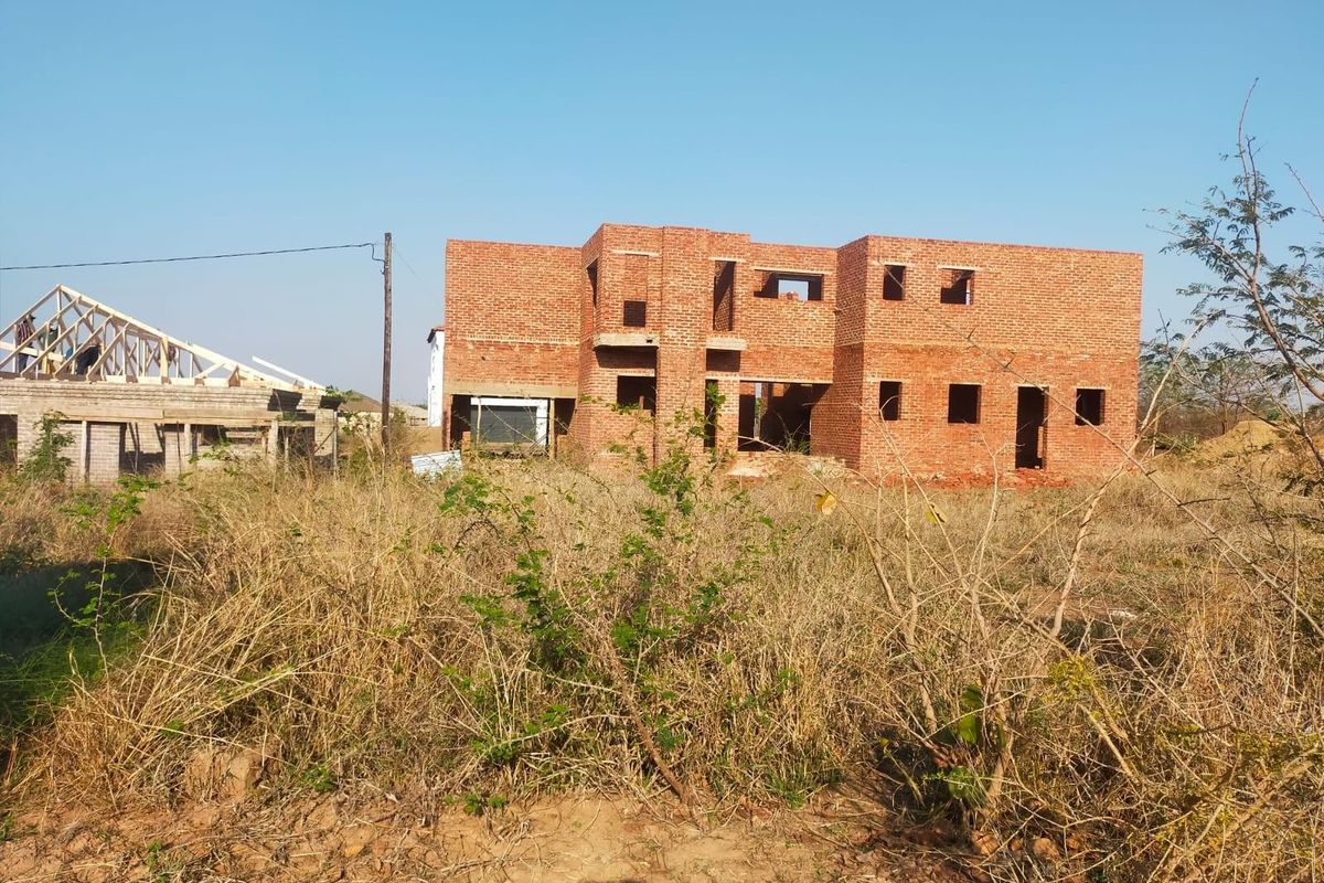 A residential property under construction featuring an exposed brick structure and timber roof trusses on a vacant plot.