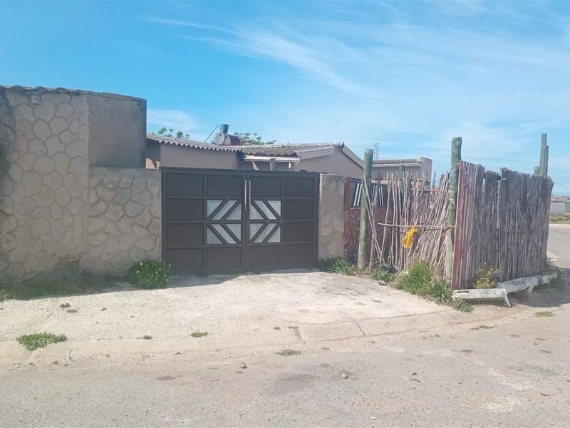 Front exterior view of the property featuring a solid metal gate, stone-textured boundary wall, and a rustic wooden fence along the street frontage.