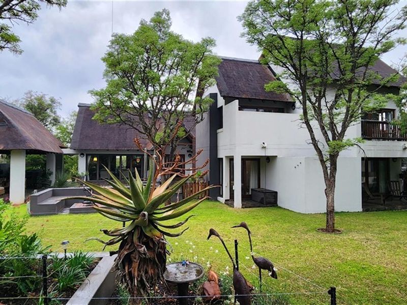 A view of the rear elevation of the house, featuring a thatched roof, a landscaped garden, and a covered patio area.