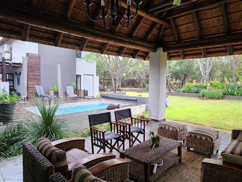 Covered patio with a thatched roof overlooking a private swimming pool and landscaped garden area.