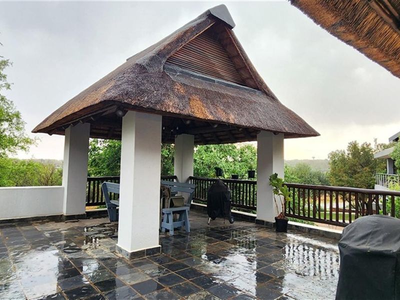 Covered outdoor patio featuring a traditional thatched roof, tiled flooring, and wooden balustrades, offering an open-air space for relaxation and entertainment.