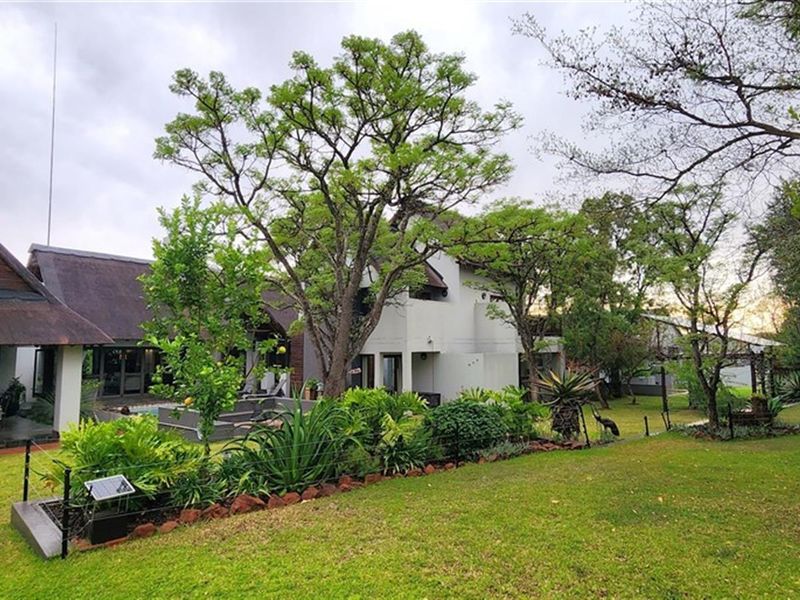 A view of the rear exterior of the house, featuring a thatched roof patio area, landscaped garden, and mature trees.