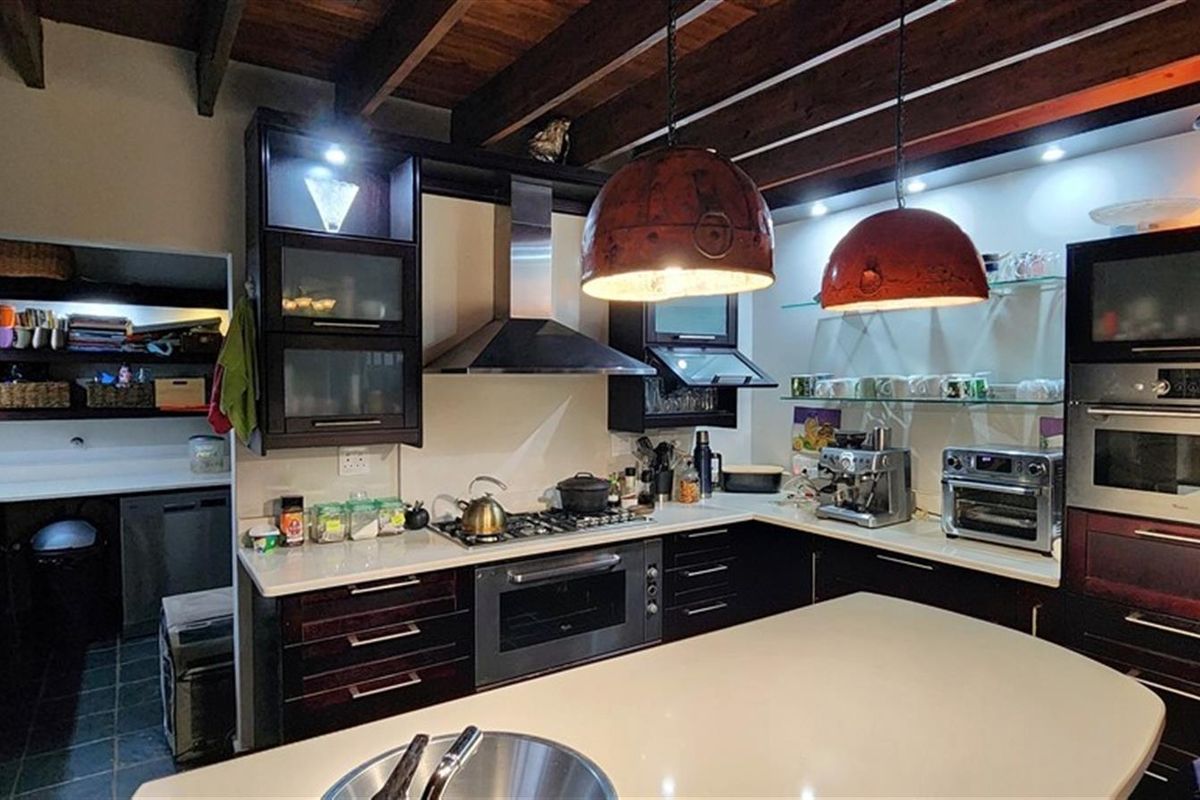 A well-appointed kitchen featuring dark cabinetry, stone countertops, a built-in oven, gas hob, extractor fan, and an adjacent scullery area with exposed timber beams.