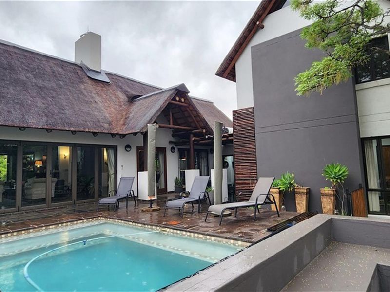 A well-maintained outdoor pool area featuring a paved deck, thatched roof architecture, and integrated patio space, ideal for relaxation and outdoor living.