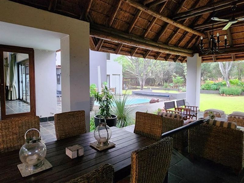 Spacious covered patio featuring a traditional thatched roof, slate flooring, and direct access to the garden and swimming pool area.