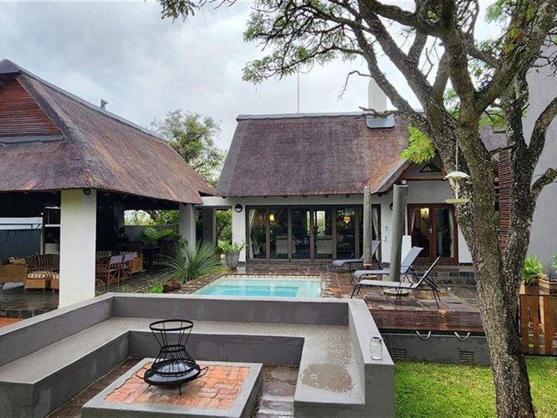 Rear garden area featuring a swimming pool, a covered patio with a thatched roof, and a built-in sunken fire pit seating area.