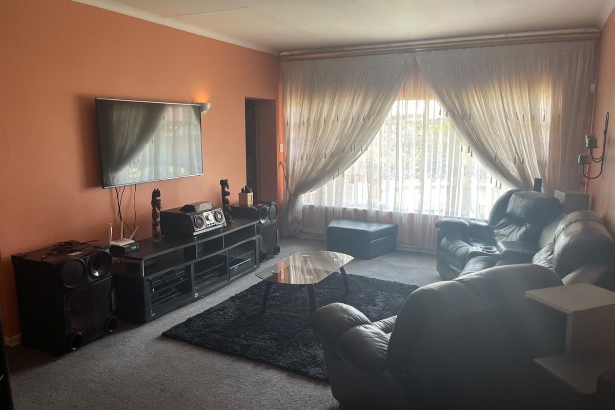 A comfortable living room featuring carpeted flooring, large windows with curtains, and wall-mounted television space.