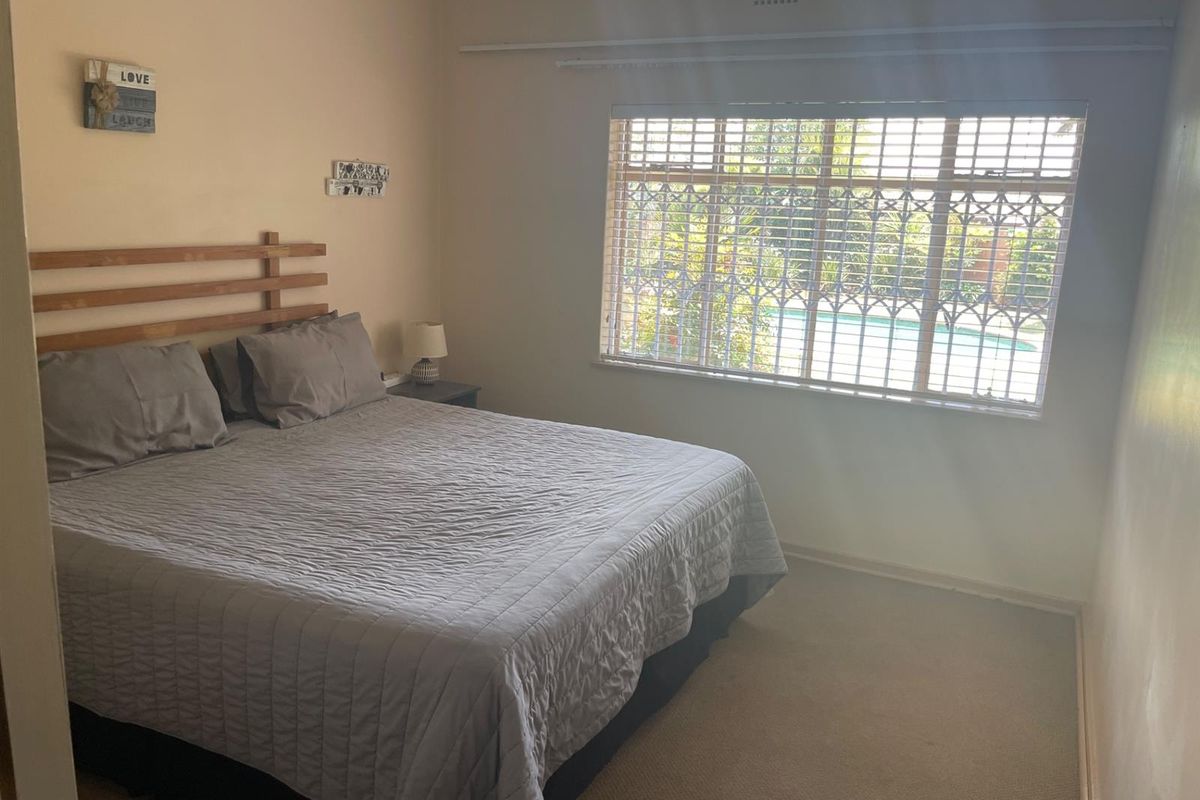A functional bedroom featuring carpeted flooring, a large window with security bars, and neutral wall finishes.