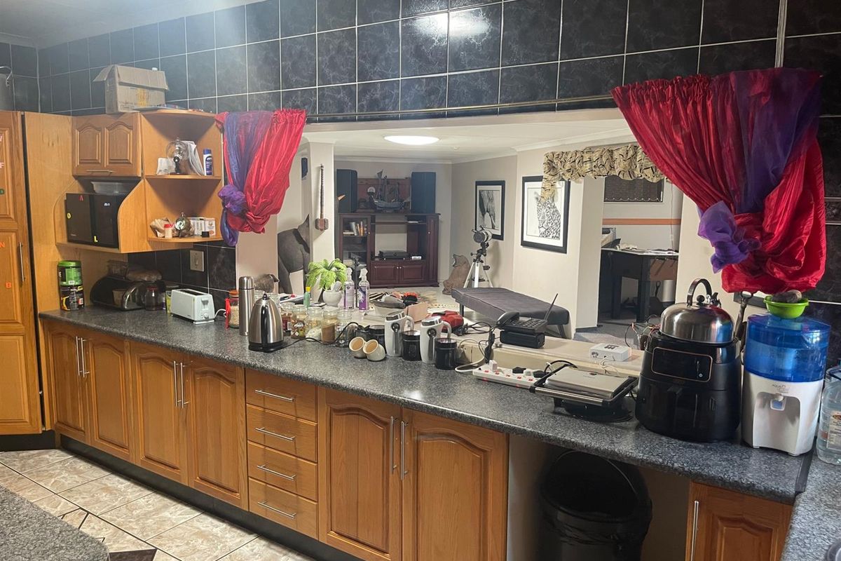 A dated kitchen featuring wooden cabinetry, dark granite-style countertops, and a pass-through window overlooking the adjacent living area.