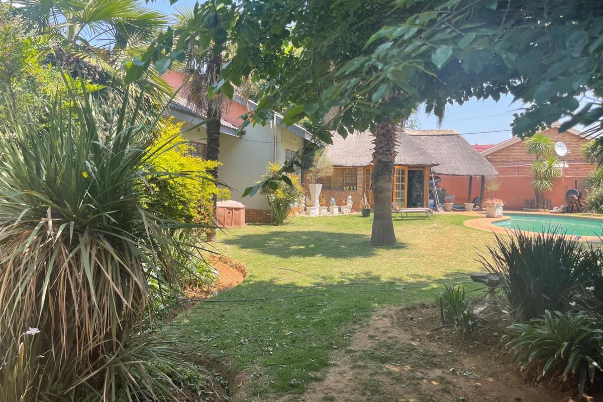 A spacious rear garden featuring a swimming pool, established palm trees, and a thatched-roof outdoor entertainment area.
